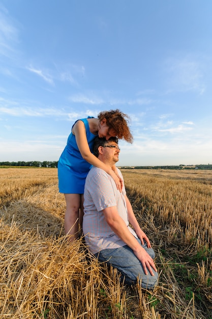 Adult farmer and wife spend time in the field. The man is sitting. A woman stands next to him and hugs him. A woman kisses her husband on the head.