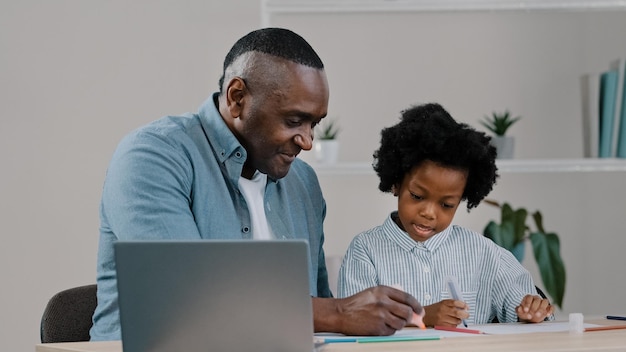 Adult father home teacher helping little daughter to do homework sit at desk in room study remote