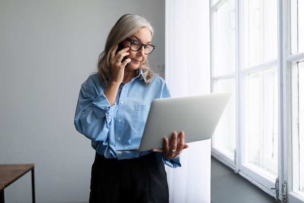 Adult fiftyyearold female business consultant speaks on a mobile phone with a laptop in her hands