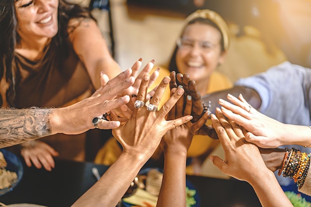 Adult friends in group sitting around the dinner table highfives all together celebrating friendship and to be united together concept of lifestyle trust unity togetherness focus on hands