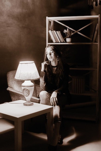 An adult girl sits in a chair near the table Black and white photo of a girl in a room