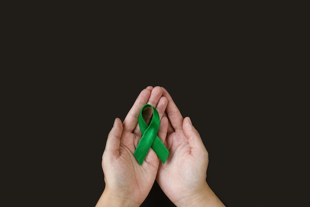 Adult hands holds green ribbon on black background World lymphoma awareness day September 15