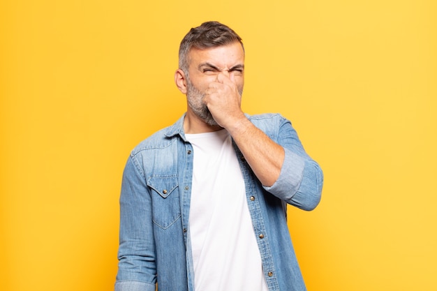 Adult handsome man feeling disgusted, holding nose to avoid smelling a foul and unpleasant stench