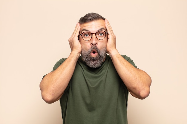 Adult handsome man looking unpleasantly shocked, scared or worried, mouth wide open and covering both ears with hands