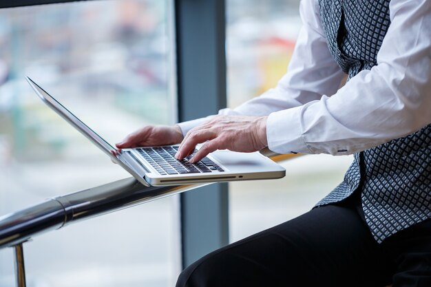 Adult male businessman, teacher, mentor working on a new project. Sits by a large window on the table. He looks at the laptop screen.