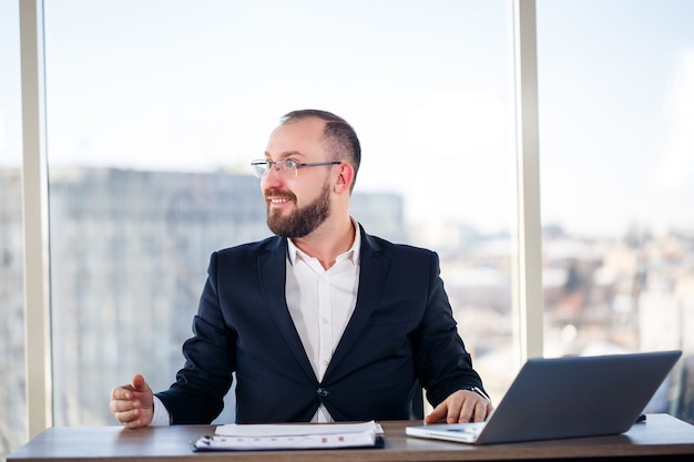 Adult male mentor, director, businessman in glasses and a suit studying documents while sitting at the table. Working day concept