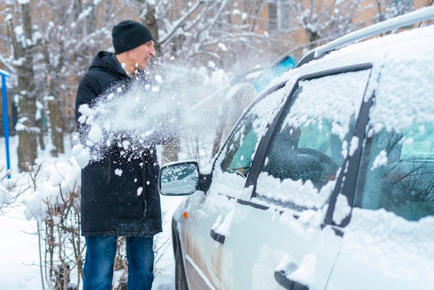 Adult male removing snow from car roof with brush in winter season