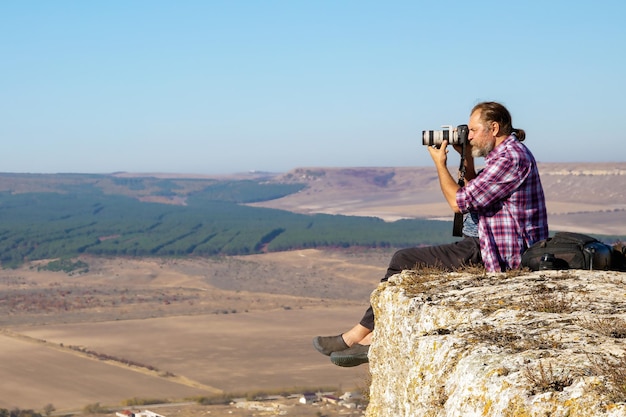 An adult male tourist photographer sits on rock and shoots landscapes