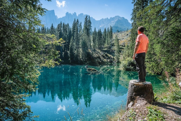 An adult man admiring the wonderful mountain scenery of the turquoise water of the moraine Carezza