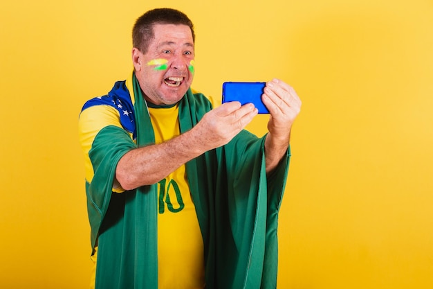 Photo adult man brazil soccer fan using flag smartphone watching game by cellphone online streaming