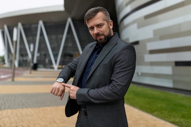 An adult man in a business suit points his finger at the clock on the background of an office