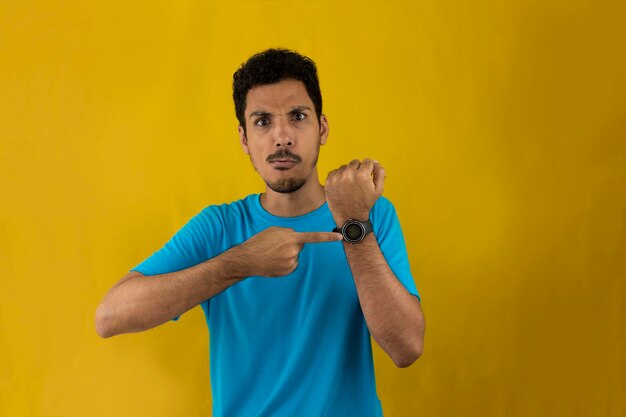 Adult man pointing at his watch on his wrist. Handsome Black Man with blue shirt on yellow.