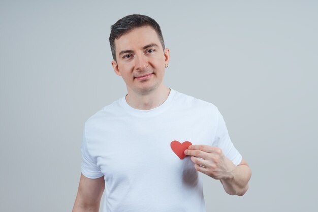 An adult man in a white T-shirt, holding a heart sign on his chest. Happy Valentine's Day. World Heart Day.