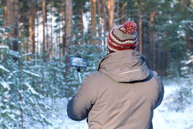 An adult man in a winter forest uses a selfie stick to shoot with a smartphone People and technology