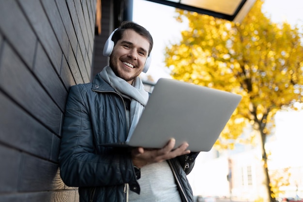 An adult man with a laptop in his hands and headphones leaning against the wall against the backdrop