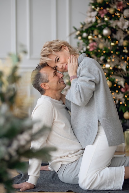 adult man and woman sit on the floor near the christmas tree and hug