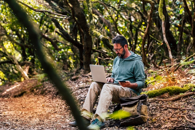 Adult man work with computer laptop in the middle of the green wild forest