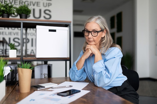 Adult mature business woman sitting at the office desk at work looking at documents accounting