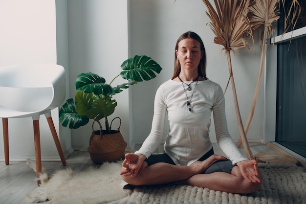 Adult mature woman doing yoga at home living room with online tutorials on laptop