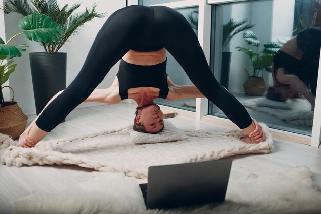 Adult mature woman doing yoga at home living room with online tutorials on laptop