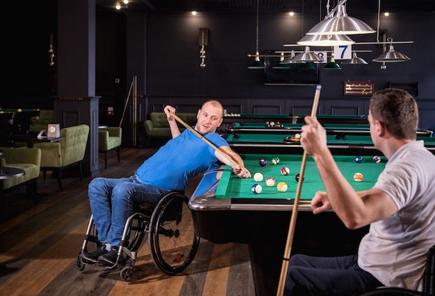 Adult men with disabilities in a wheelchair play billiards in the club