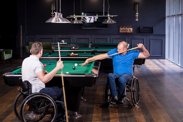 Adult men with disabilities in a wheelchair play billiards in the club