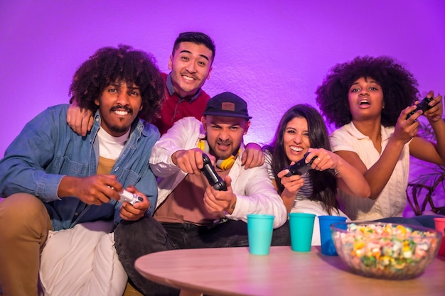 Adult party Attractive young men sitting on the sofa playing video games with popcorn Expressing joy while holding the joystick and looking at the monitor