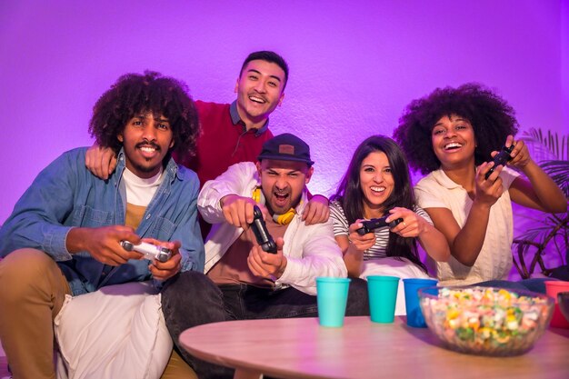 Adult party Attractive young men sitting on the sofa playing video games with popcorn Expressing joy while holding the joystick and looking at the monitor