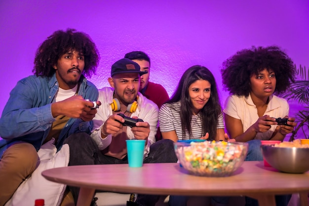 Adult party Young people sitting on the sofa playing video games with popcorn Joystick or controller in hand purple led playing racing games