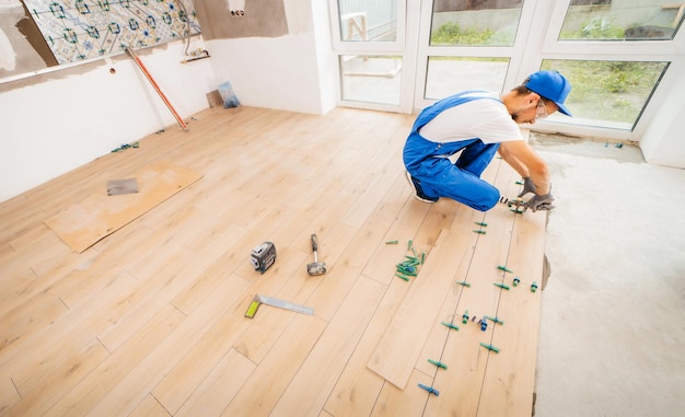 Adult repairman in a special uniform laying tiles with tile leveling system on the floor in a new ho