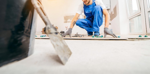 Adult repairman in a special uniform laying tiles with tile leveling system on the floor in a new ho