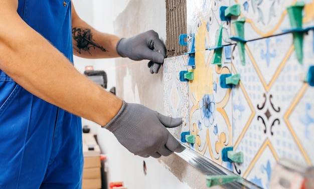 Adult repairman in a special uniform laying tiles with tile leveling system at wall on kitchen in a