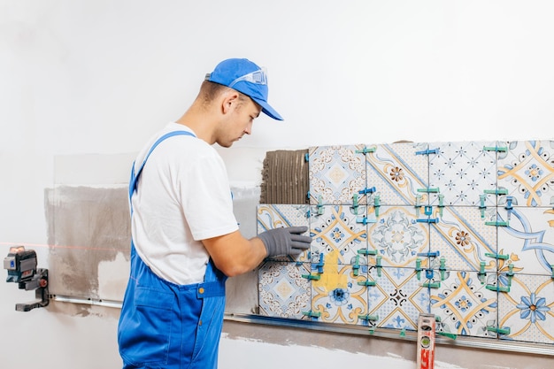 Adult repairman in a special uniform laying tiles with tile leveling system at wall on kitchen in a