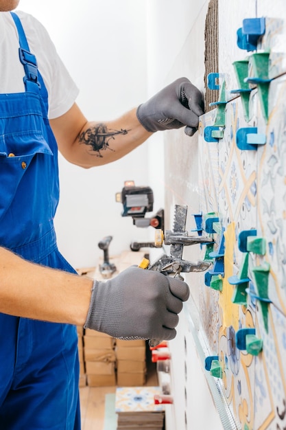 Adult repairman in a special uniform laying tiles with tile leveling system at wall on kitchen in a