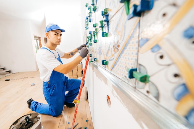 Adult repairman in a special uniform laying tiles with tile leveling system at wall on kitchen in a