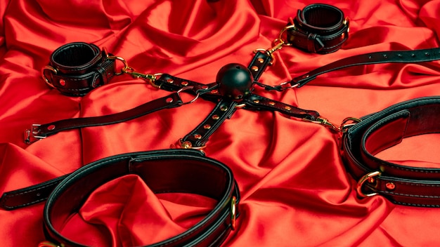 Photo adult sex games bdsm items leather straps handcuffs and gag ball on a red satin sheet