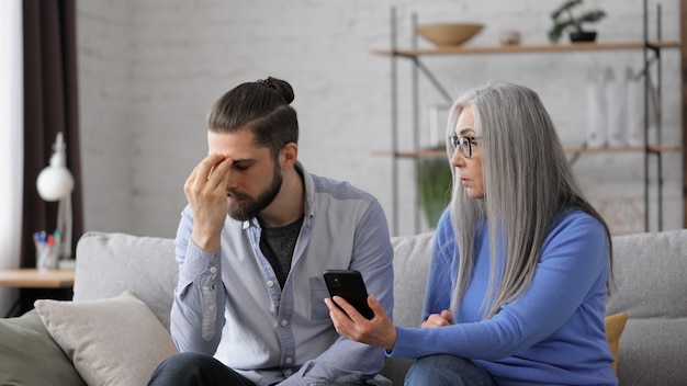 Adult son teaching his senior mother to use smartphone mobile apps sharing photos shopping online