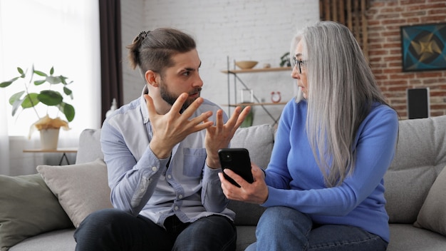 Adult son teaching his senior mother to use smartphone mobile apps sharing photos shopping online