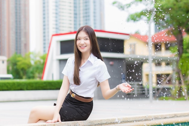 Adult Thai student in university student uniform Asian beautiful girl sitting shake the water