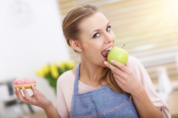 Adult woman choosing between healthy and unhealthy snack in the kitchen