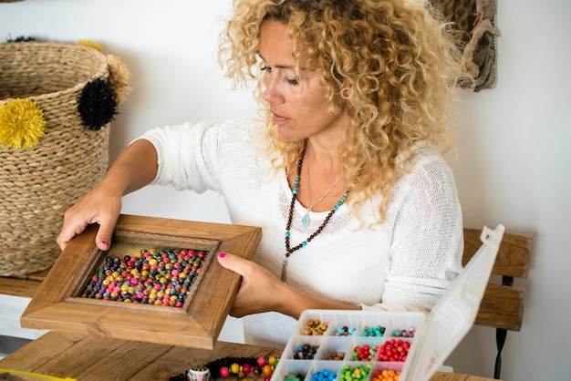 Adult woman doing hand made creations jewelry at home with colorful beads and cords