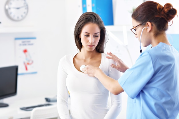 adult woman having a visit at female doctor's office and being examined with stethoscope