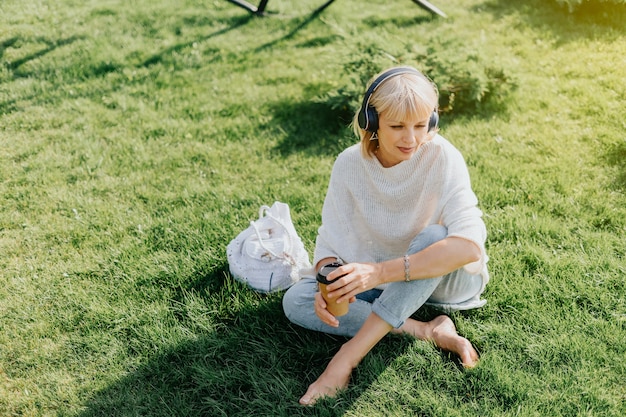 Adult woman in headphones sitting on the grass outside in park