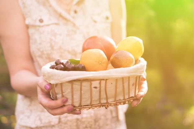 Adult woman holding a crate with fresh new season harvest in the garden