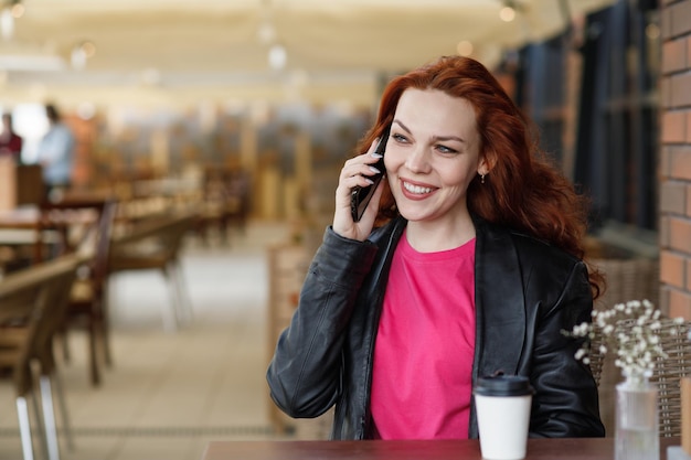 Adult woman is sitting in a cafeveranda with a cup of coffee and communicates on a mobile phone