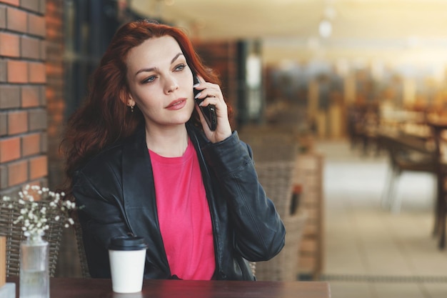 Adult woman is sitting in a cafeveranda with a cup of coffee and communicates on a mobile phone