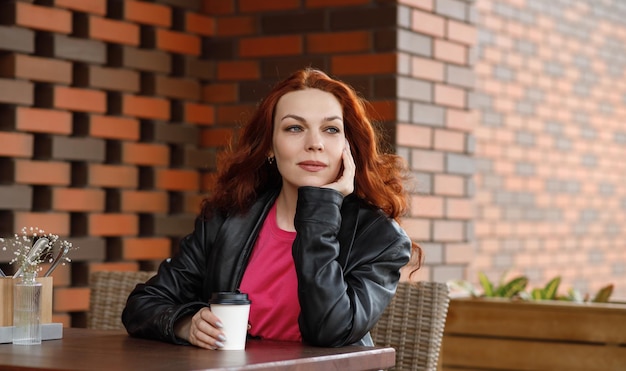 An adult woman is sitting in a summer cafe with a cup of coffee and smiling