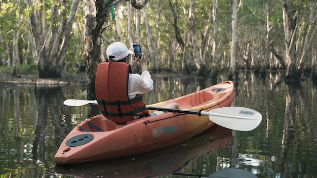 adult woman kayaking canoe boat on lake she take photo natural scenery by smartphone on summer day