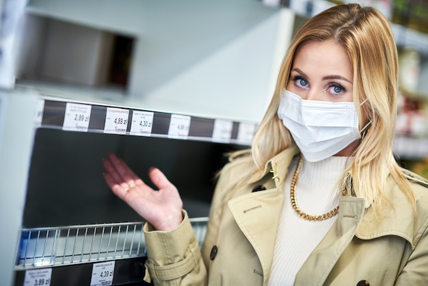 adult woman in medical mask in front of empty shelves in grocery store