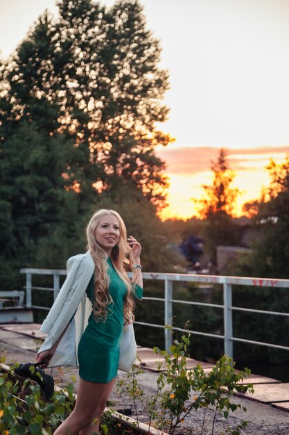 Adult woman on nature walking in summer forest on railway of dusk. Dreamer lady in dress walk evening on railroad. Positive emotion female on rails at dawn